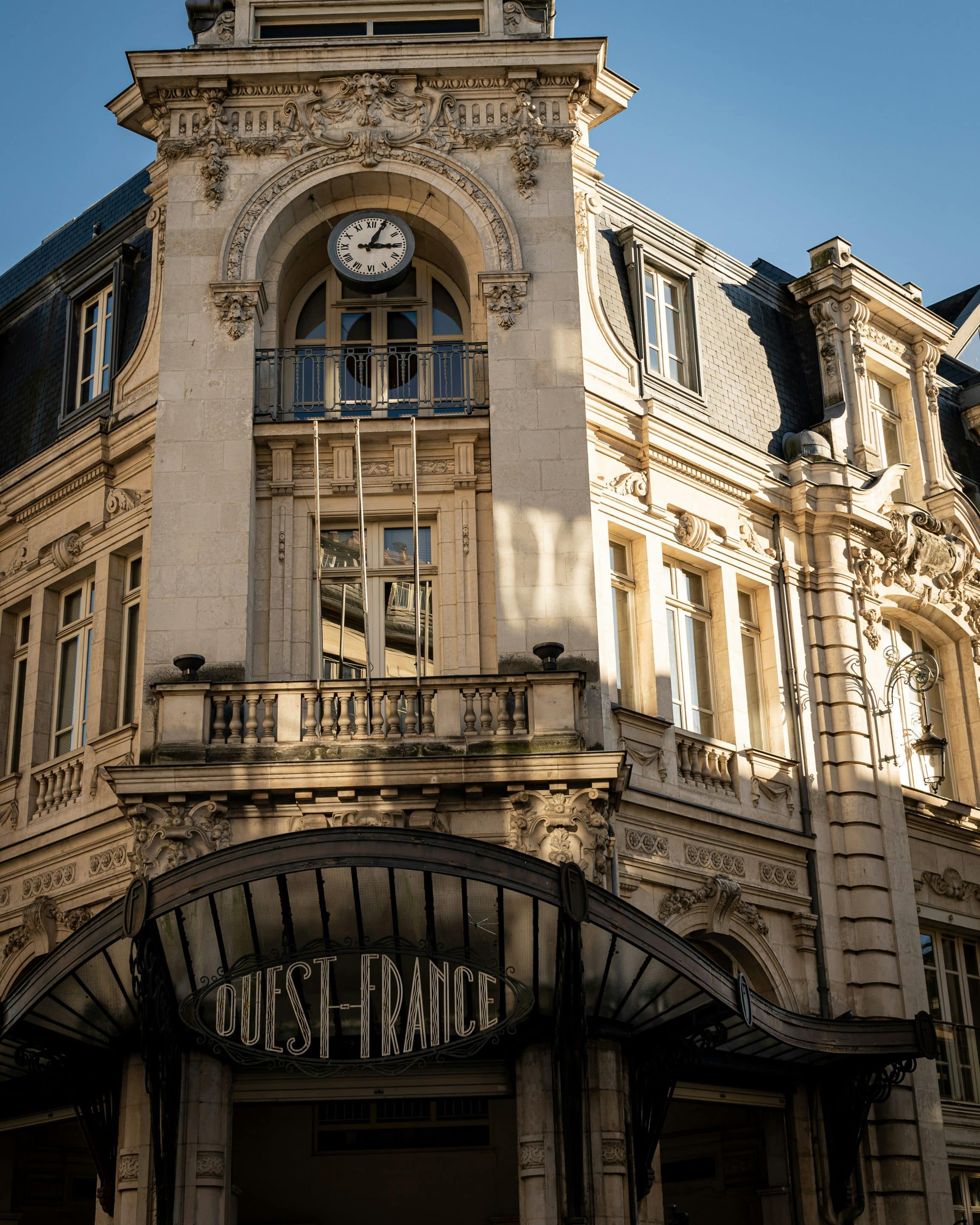 Bâtiment historique avec grandes fenêtres, horloge et marquise au dessus de l'entrée. Patrimoine secret à Rennes.